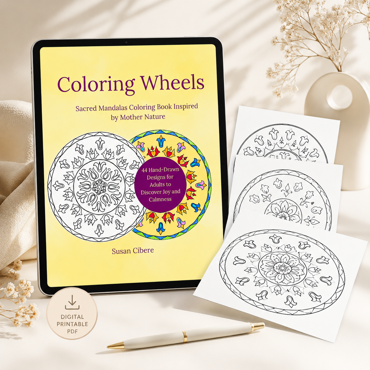 A digital coloring book cover titled 'Coloring Wheels' by Susan Cibere, shown on a tablet screen with three printed coloring pages and a gold pen arranged on a light beige surface with soft fabric and dried flowers.