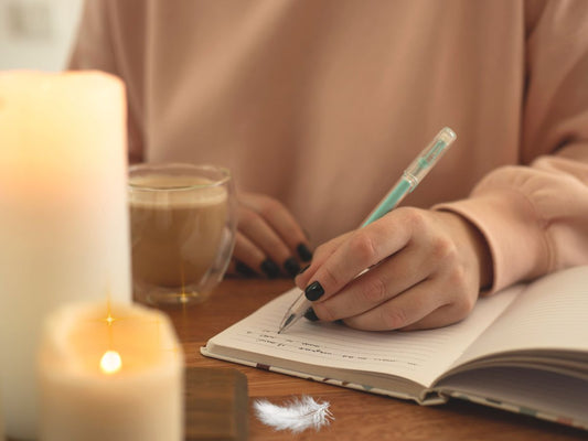 a journaling woman sitting at the table with two candles and an angelic feather the divine ginger blog